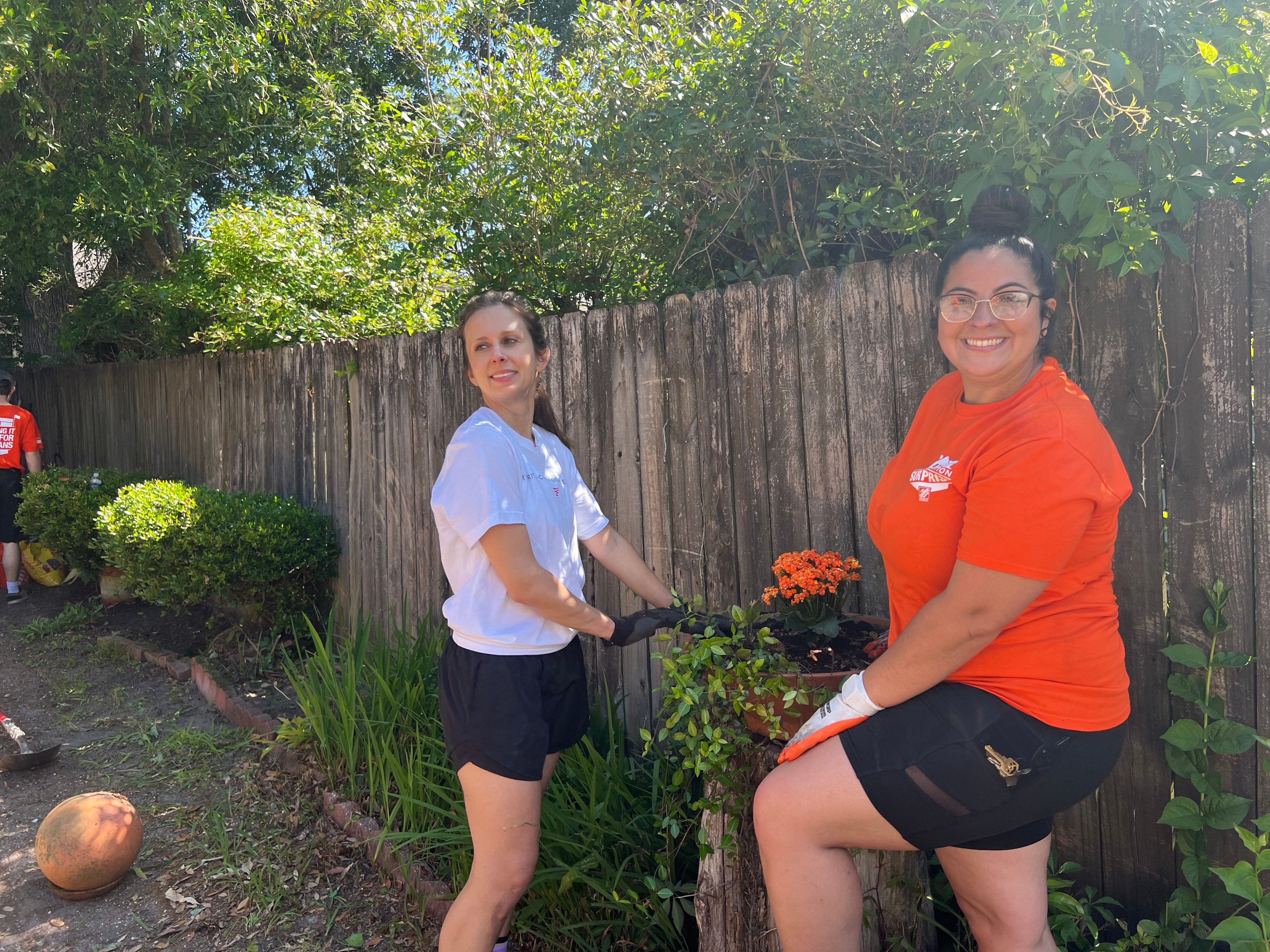 Two volunteers planting orange flowers along a fence during the service day