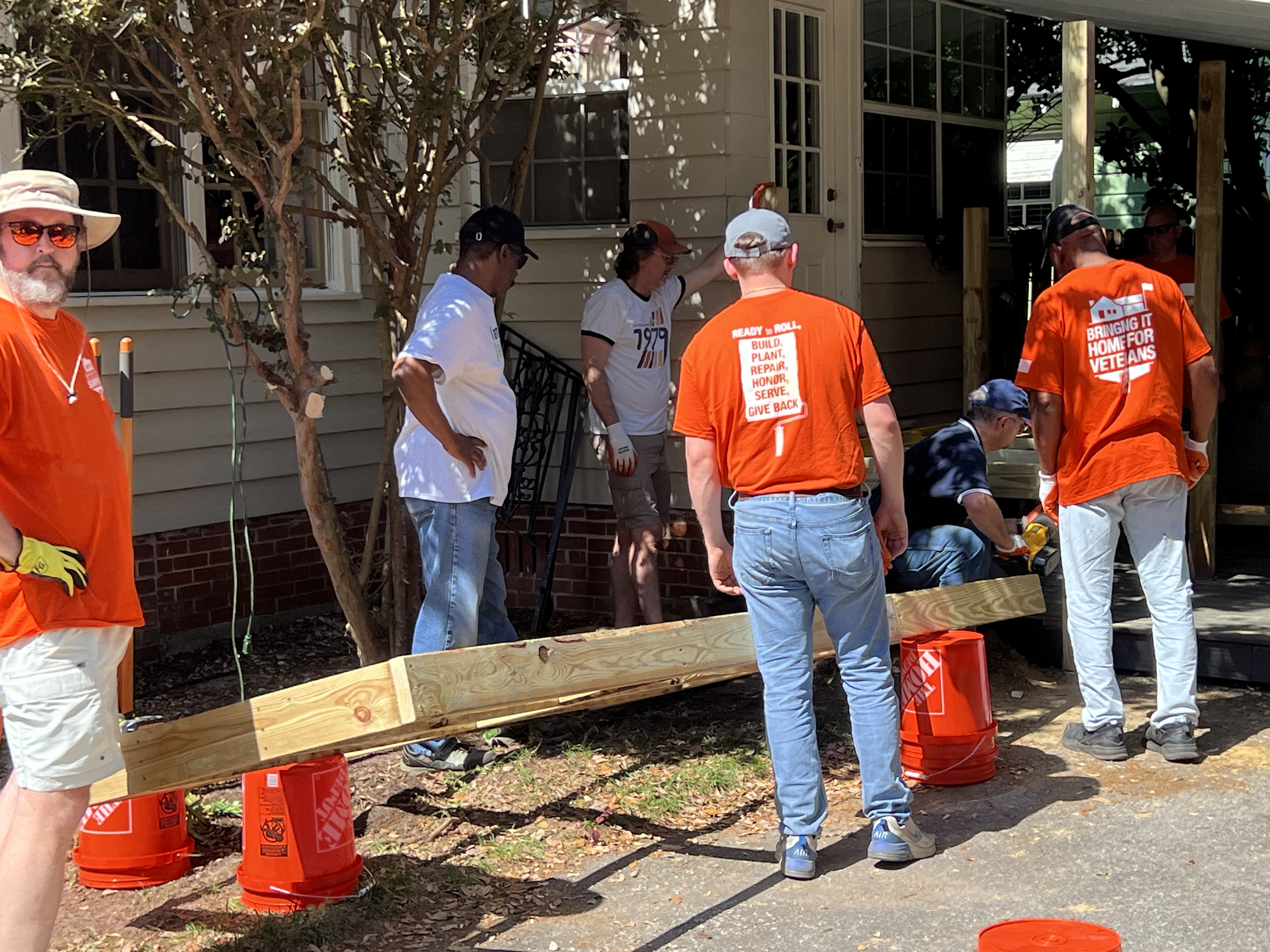 Home Depot volunteers in orange "Bringing It Home for Veterans" shirts carrying lumber for a build project