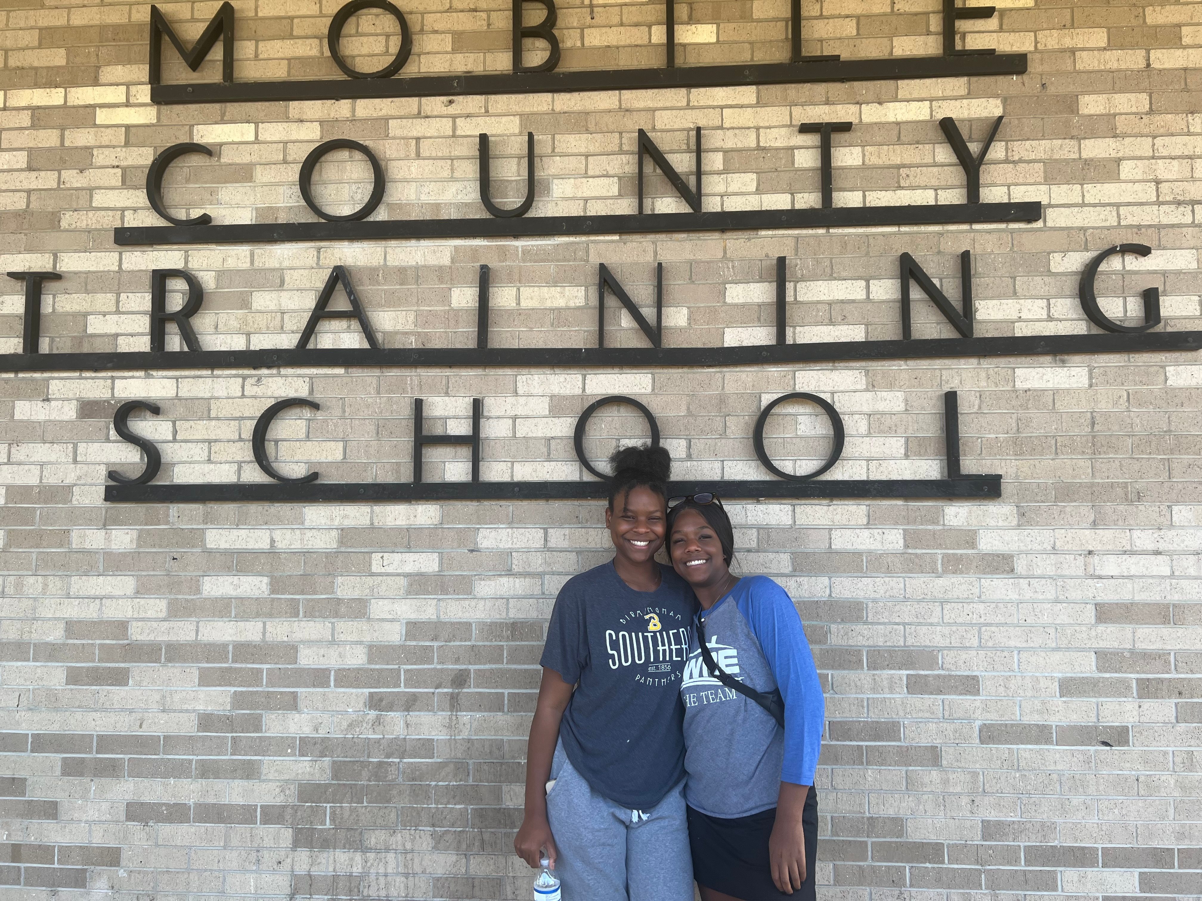 Two students smiling in front of the Mobile County Training School sign