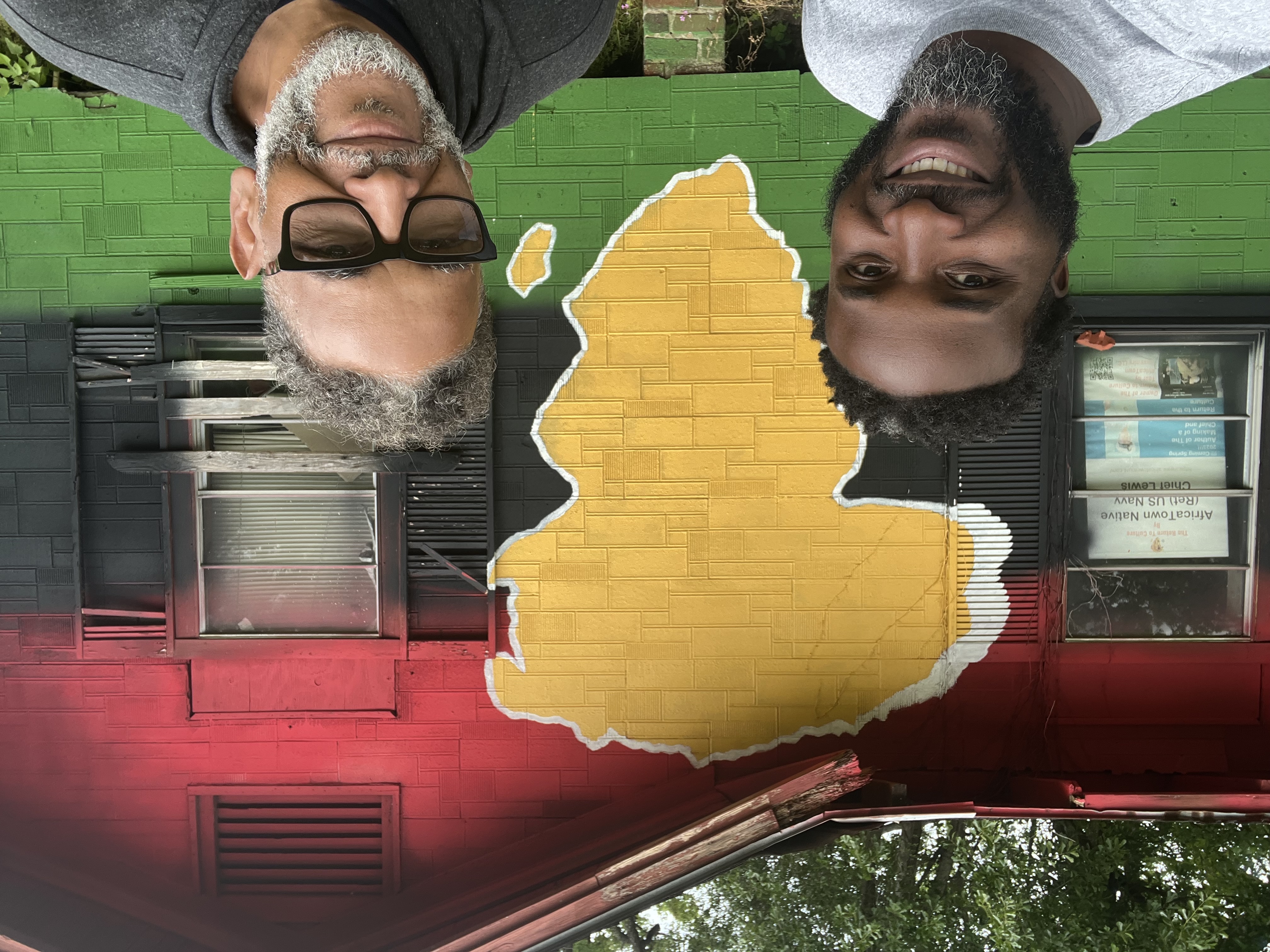 Two men taking a selfie in front of the Pan-African Return to Culture house mural