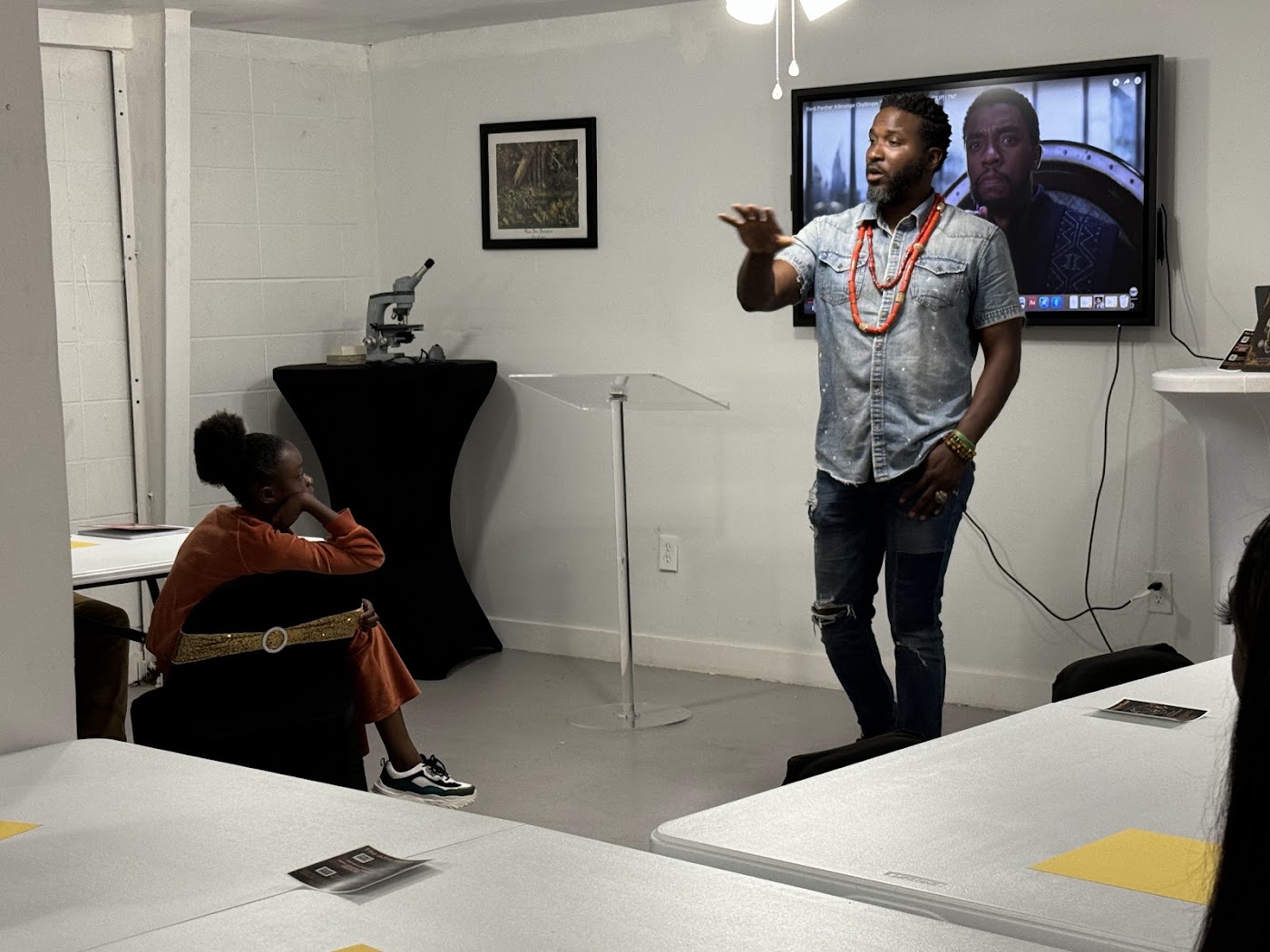 A young student listens attentively during a STEAM presentation beside a microscope station